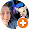 A person smiles while sitting next to a small dog with its tongue out. Both are in a car. The photo is framed with a circular border, and a star icon is visible in the bottom right corner.
