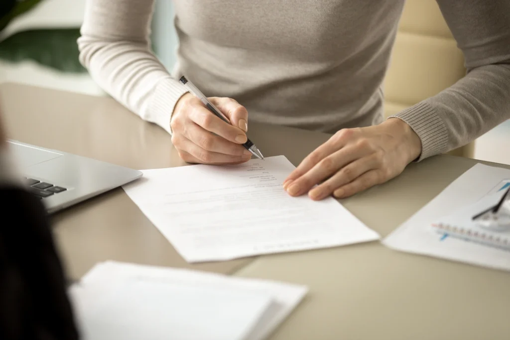 A close-up of a homeowner sitting at a bright desk and carefully signing a comprehensive roof warranty agreement with a pen, ensuring long-term peace of mind and protection for their recent exterior upgrade.