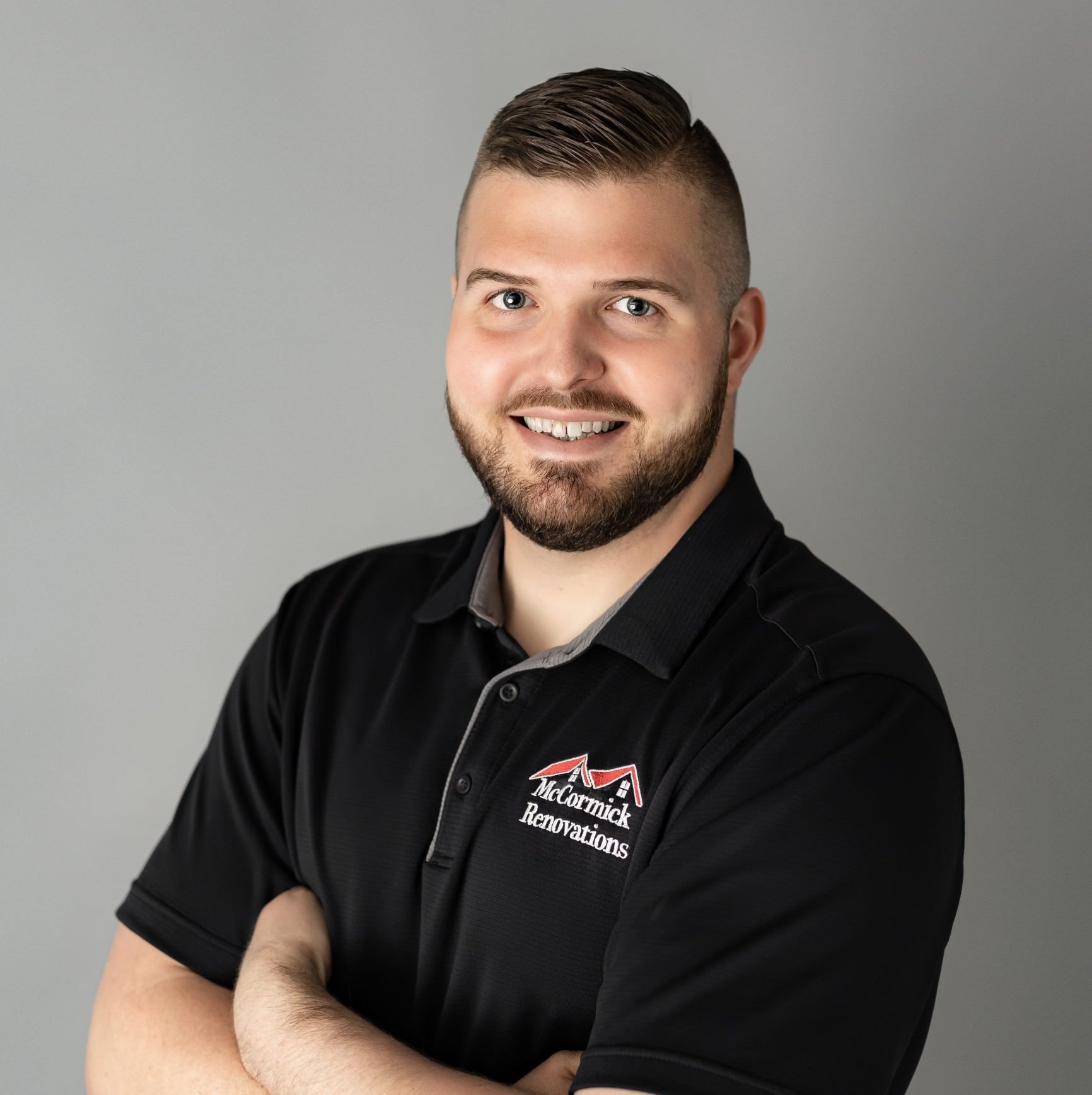 A man with a beard and short hair, smiling and dressed in a black polo shirt with a logo that reads 