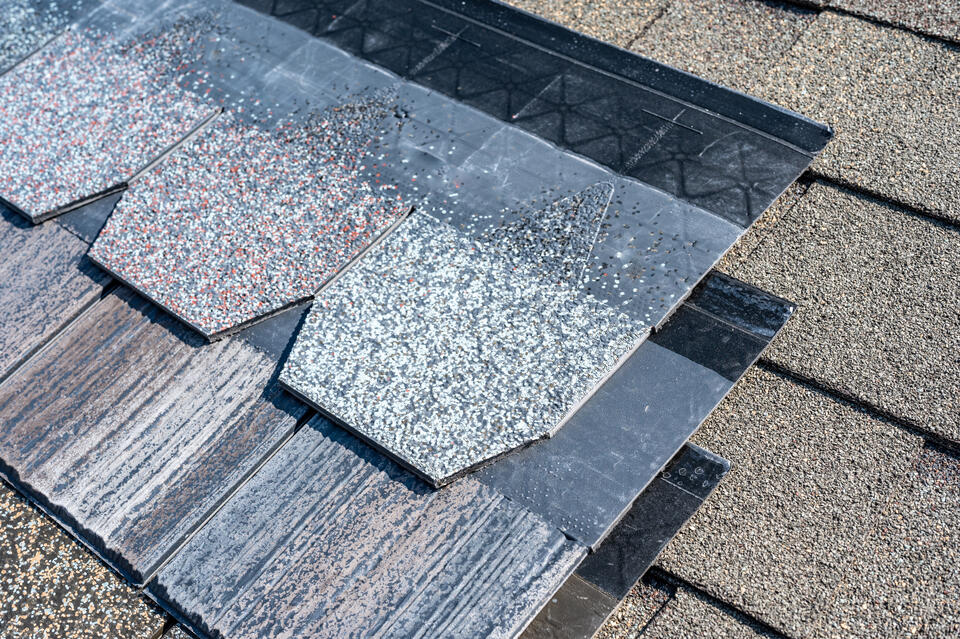 Close-up of asphalt shingles layered on a roof, featuring a variety of colors and textures. The overlapping pattern showcases both darker and lighter shades, providing a contrast against the existing roof surface.