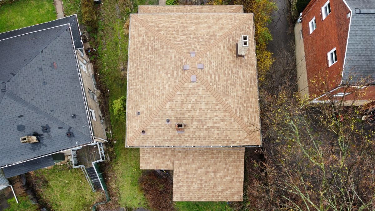 Aerial view of a tan-shingled house roof with multiple vents and a chimney