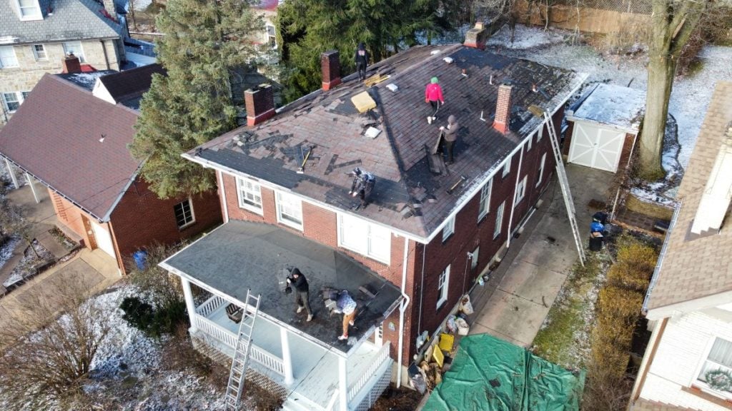 Aerial view of several people repairing the roof of a two-story brick house