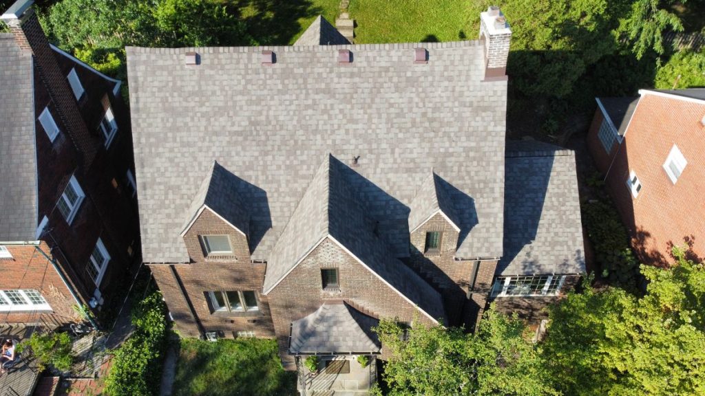 Aerial view of a large, dark brick house with a gray, multi-gabled roof