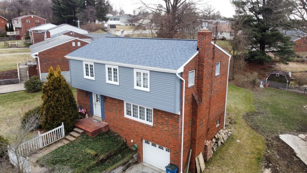 A two-story red brick house with blue siding on the upper level, white trim, and a gray shingle roof