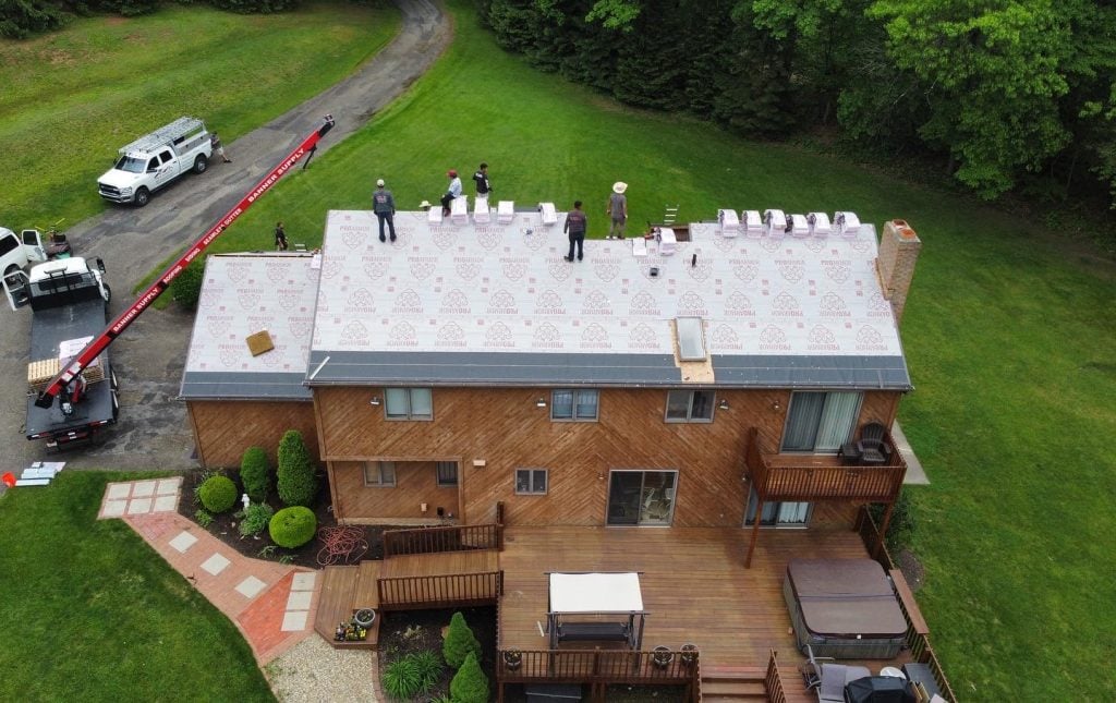 Aerial view of workers installing roofing materials on a large two-story house