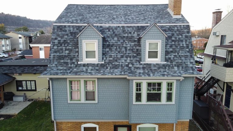 A two-story house with a shingled gray-blue mansard roof and dormer windows