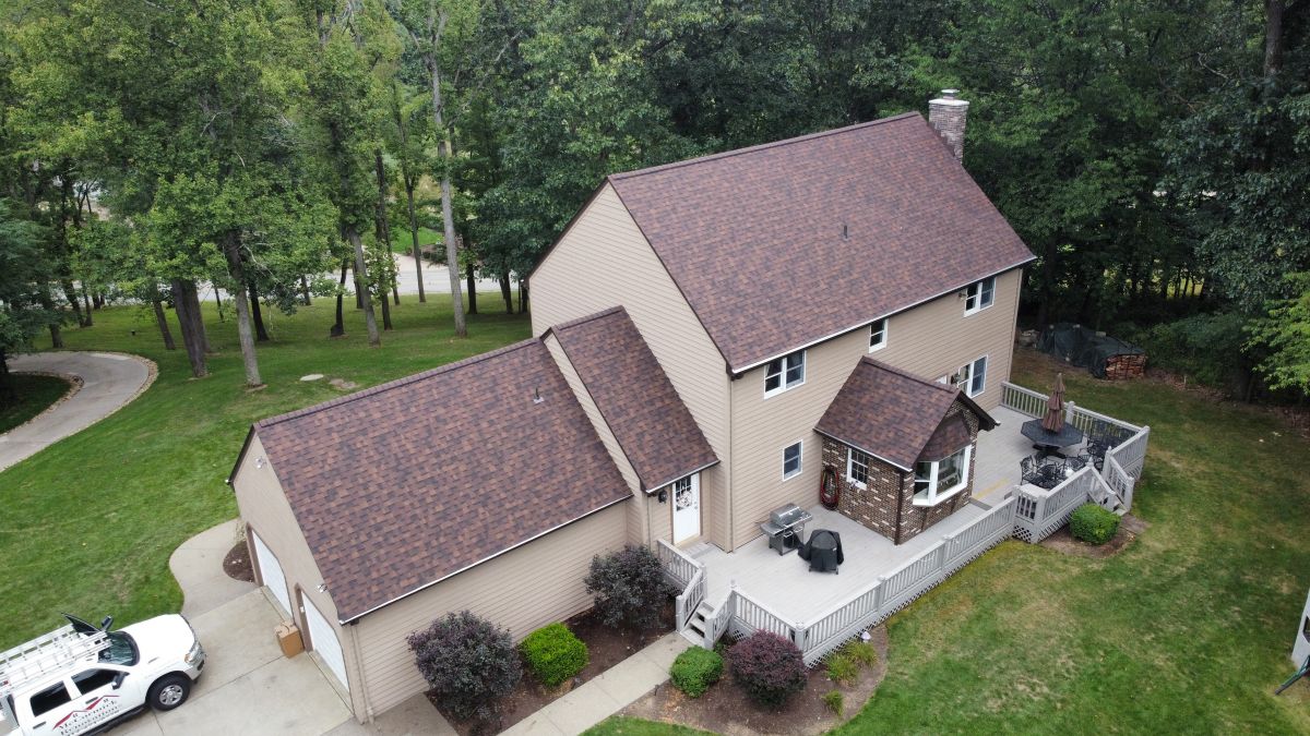 Aerial view of a two-story tan house with a brown roof, attached garage, and spacious deck
