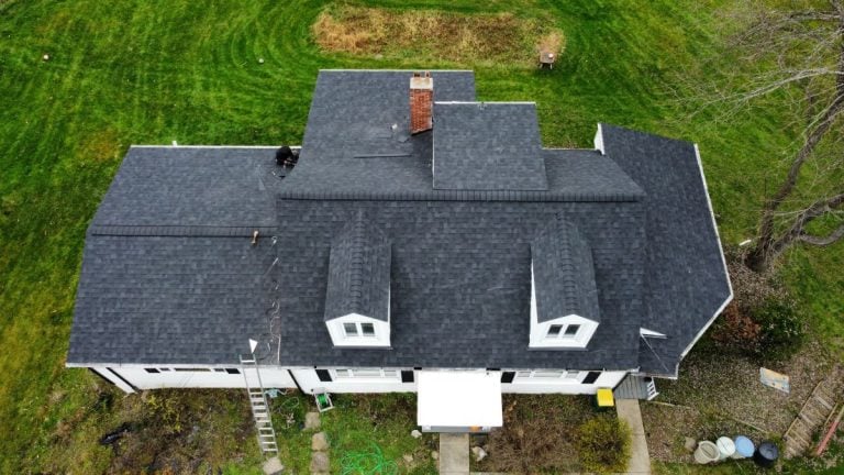 Aerial view of a house with dark gray shingles, two dormer windows, and a chimney