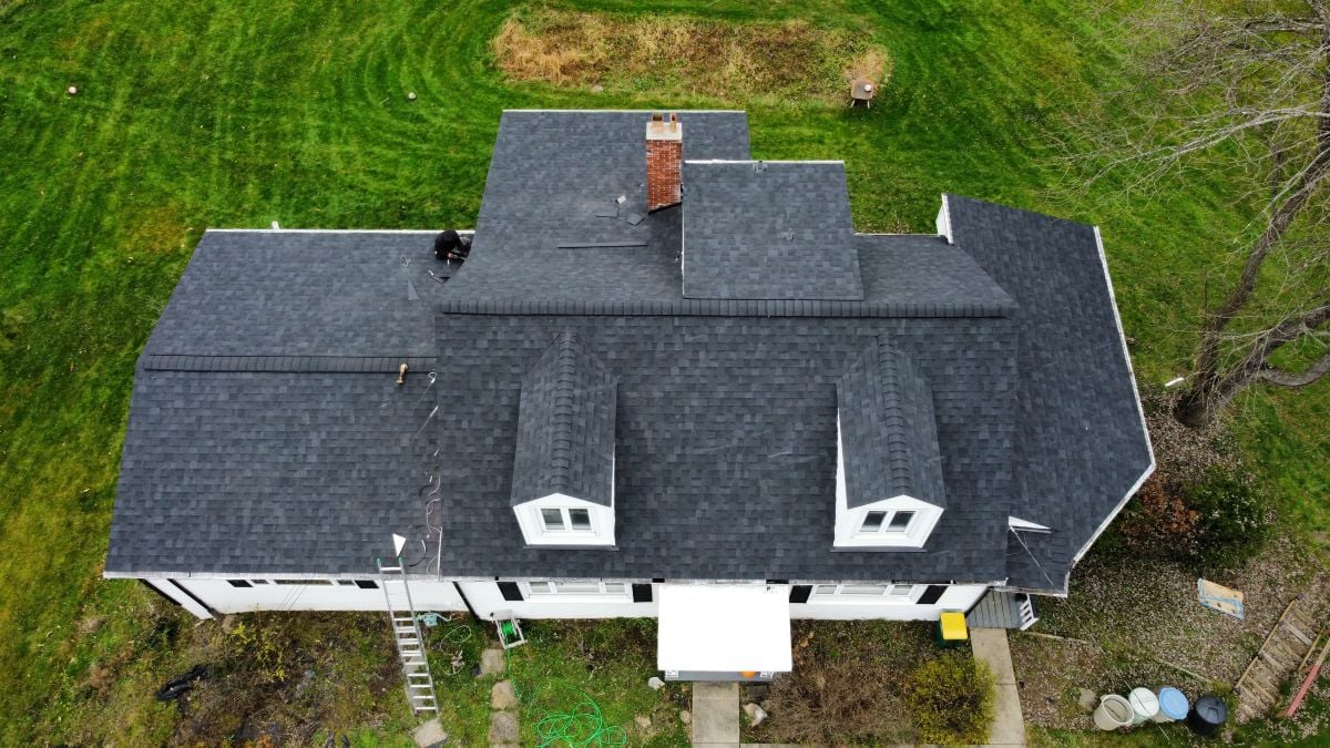 Aerial view of a house with dark gray shingles, two dormer windows, and a chimney