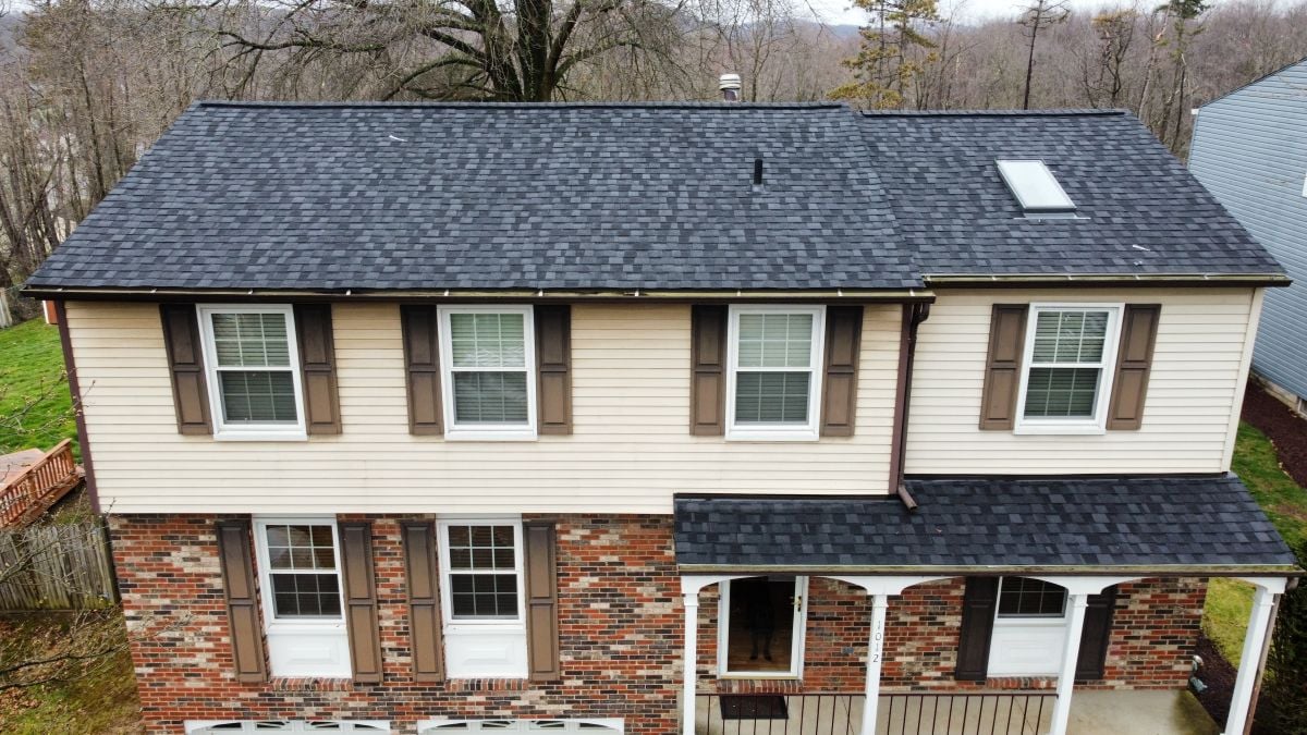 Two-story house with beige siding and red brick on the lower level, brown shutters, and a dark gray shingled roof