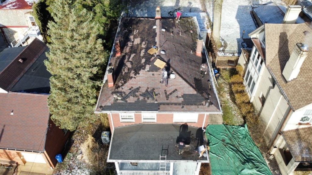 Aerial view of workers repairing a roof on a two-story house, with roofing materials scattered on the roof