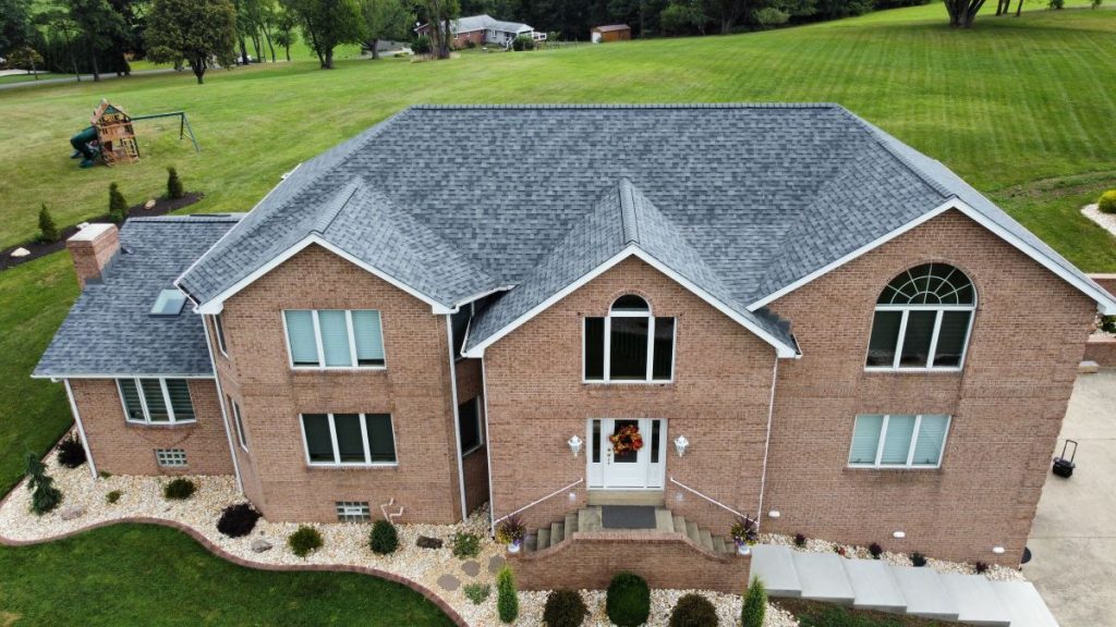 A large two-story brick house with a gray shingled roof, arched and rectangular windows