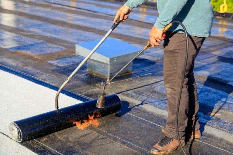torch down roofing worker holding hose with fire to paste bitumen