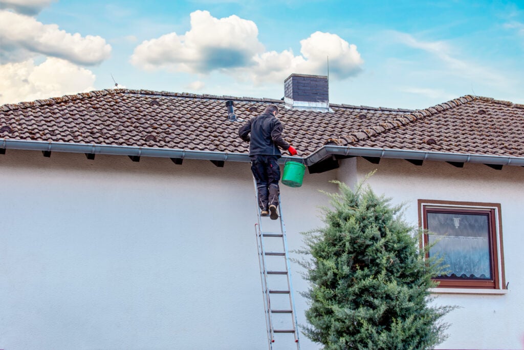 gutter maintenance worker standing on top of ladder cleaning water system