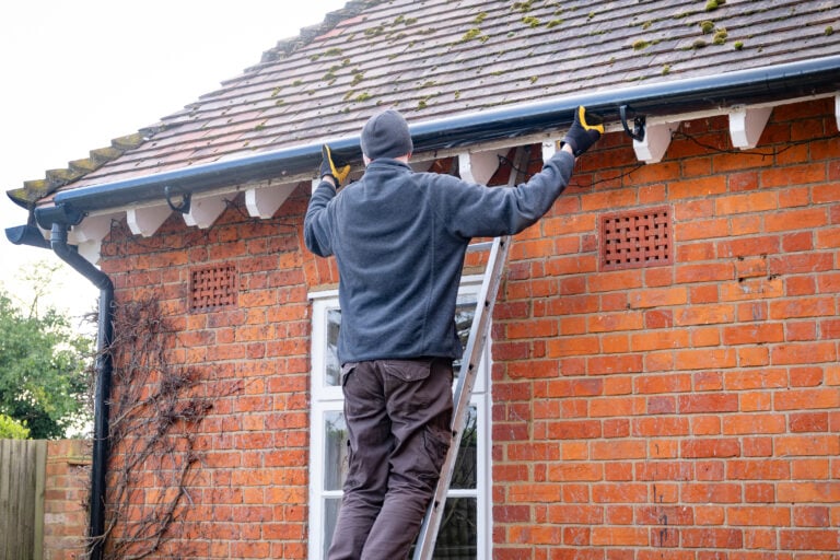gutter maintenance Man on a ladder fixing fitting a rain gutter on the eaves of a UK house