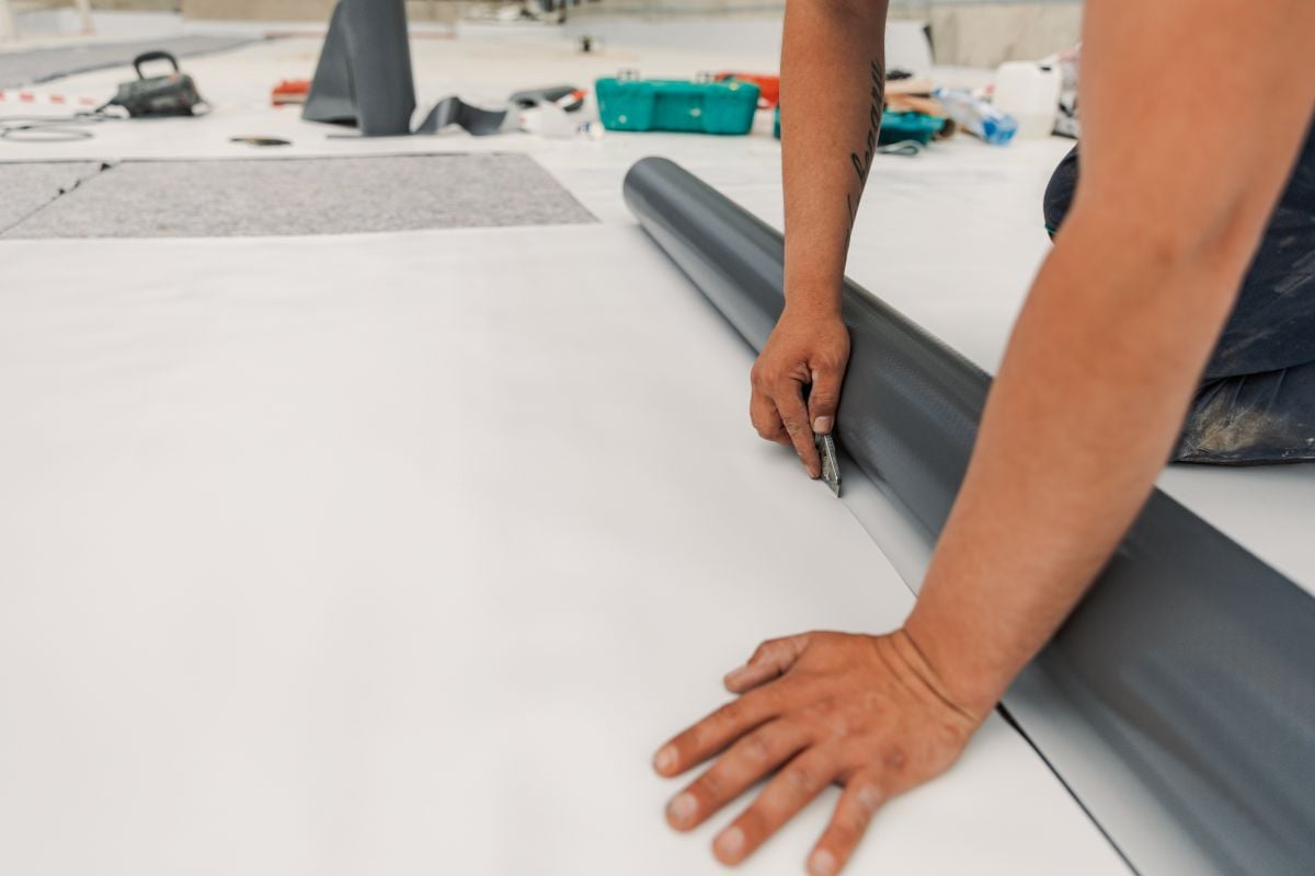 TPO roofing installation hand using heating gun roller aside