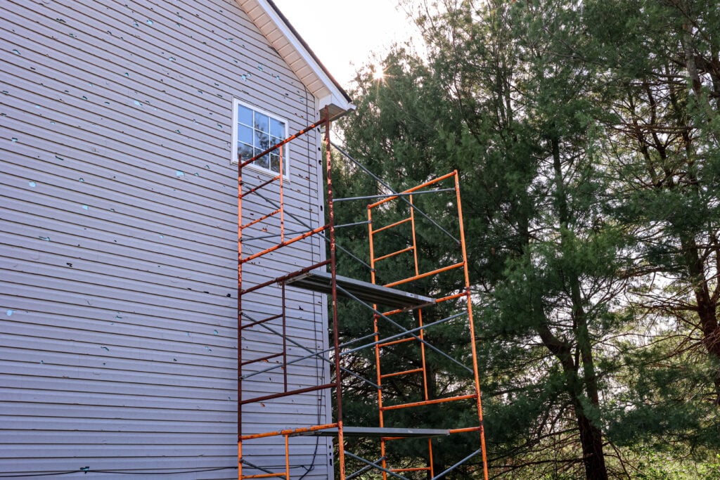 hail damage siding Scaffold On The Side of A House To Repair Vinyl Siding