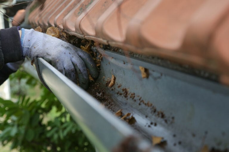 clogged gutters glove removing debris from gutter