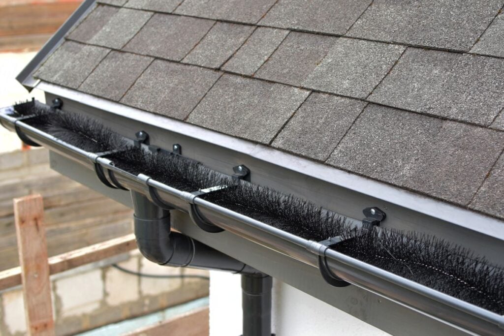 Plastic guard brush in new dark grey plastic rain gutter on asphalt shingles roof