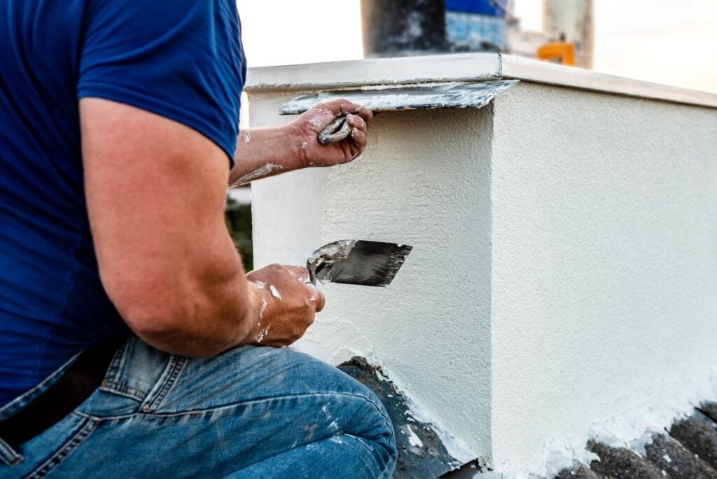 Worker applying white seamless concrete pebble-dash plaster on chimney