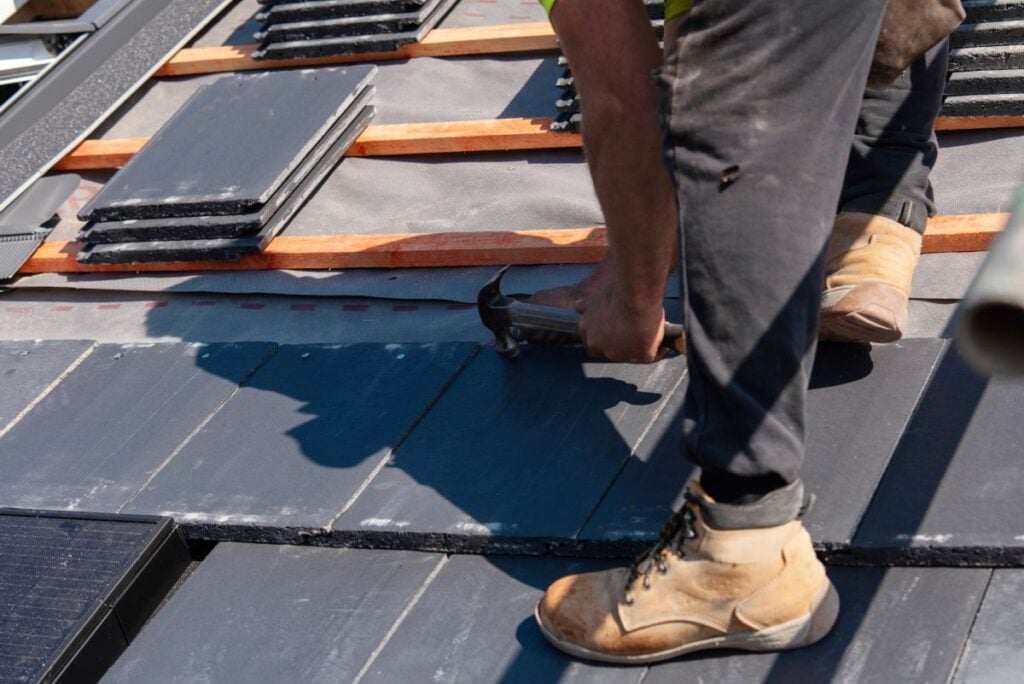 Construction worker installing slate roofing tiles on a sunny day at a residential building in the afternoon