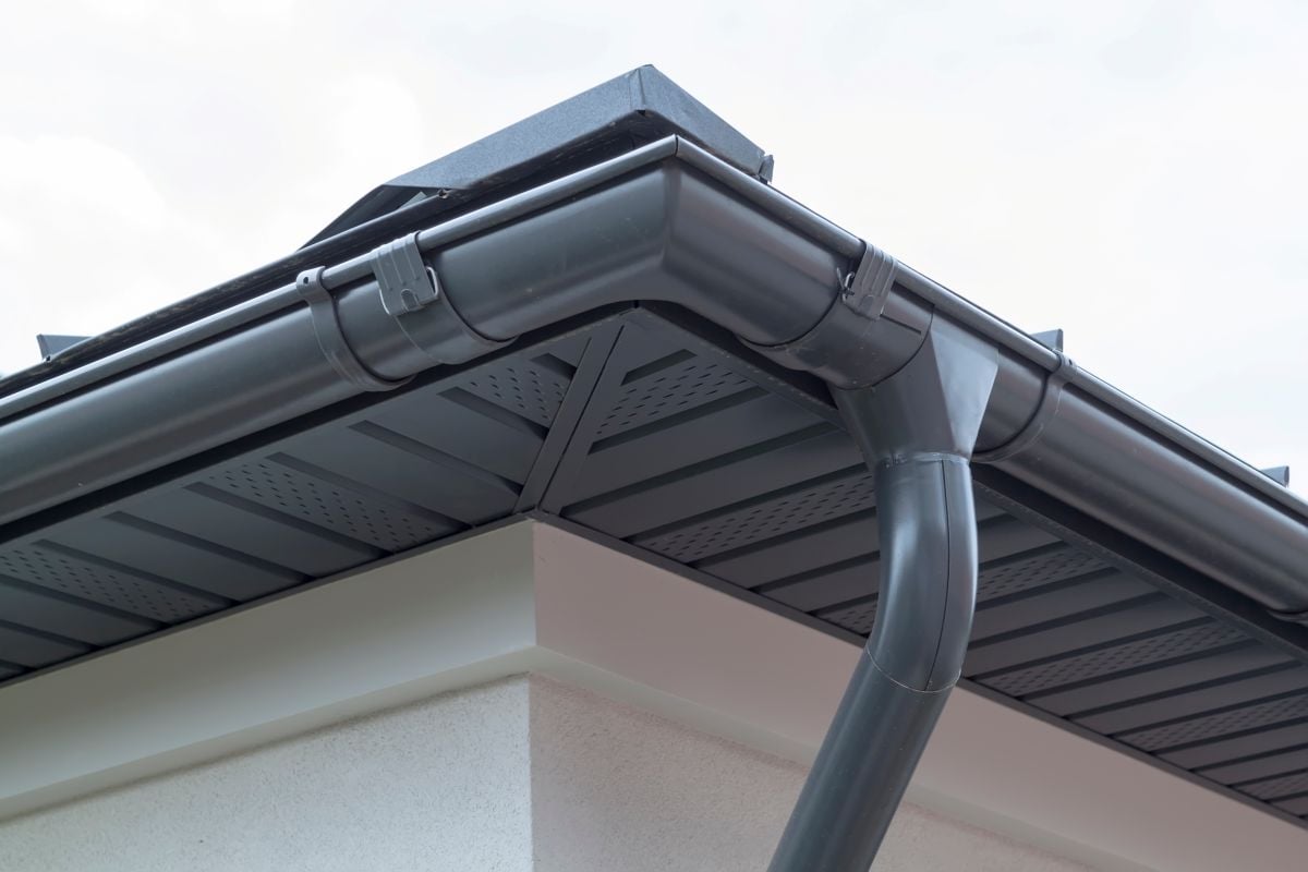 Corner of house with new gray metal tile roof and rain gutter